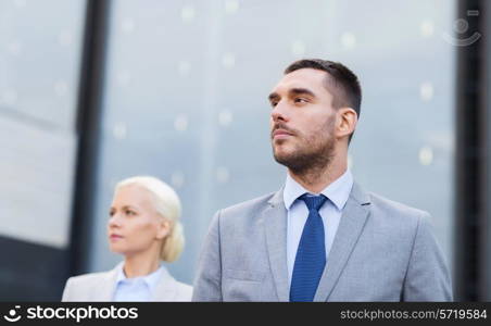 business, partnership, success and people concept - close up of serious businessman and businesswoman standing over office building