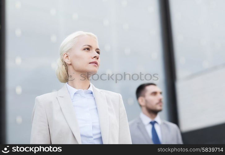 business, partnership, success and people concept - close up of serious businessman and businesswoman standing over office building