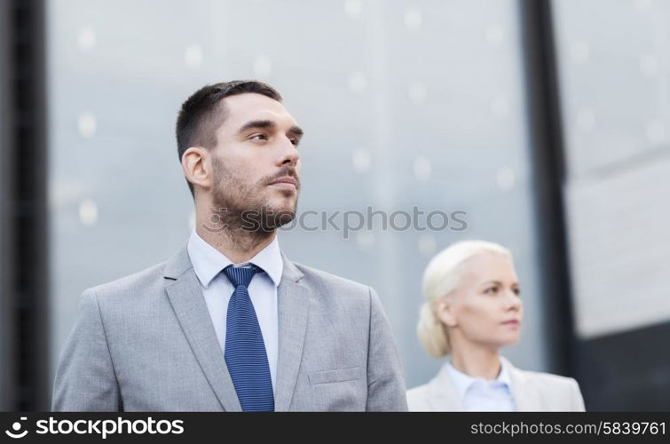 business, partnership, success and people concept - close up of serious businessman and businesswoman standing over office building