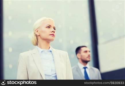 business, partnership, success and people concept - close up of serious businessman and businesswoman standing over office building