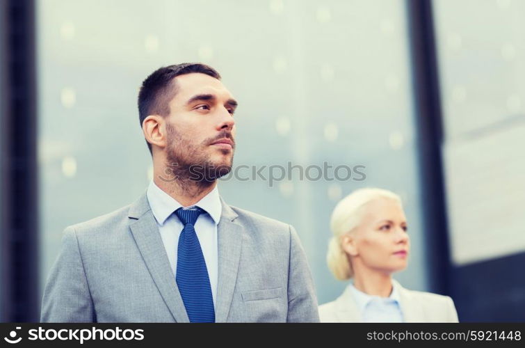 business, partnership, success and people concept - close up of serious businessman and businesswoman standing over office building