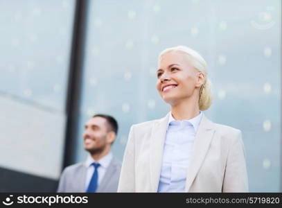 business, partnership, success and people concept - close up of smiling businessman and businesswoman standing over office building