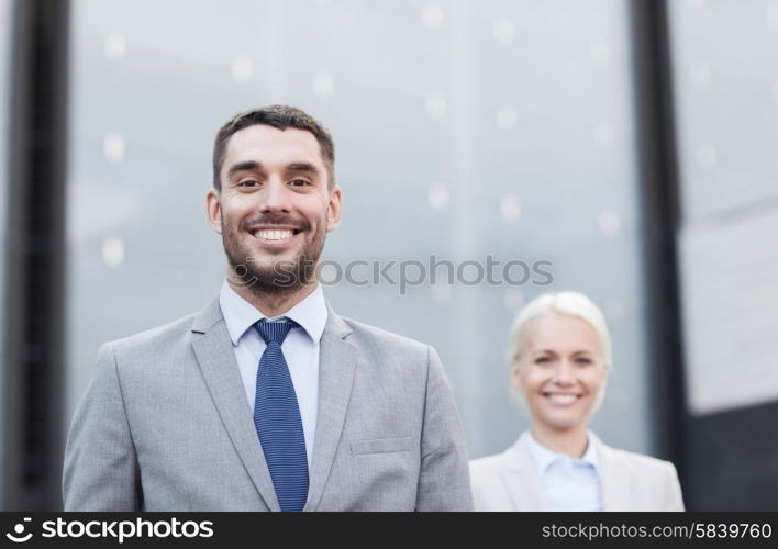 business, partnership, success and people concept - close up of smiling businessman and businesswoman standing over office building