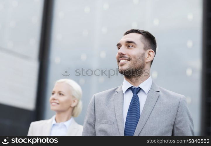 business, partnership, success and people concept - close up of smiling businessman and businesswoman standing over office building