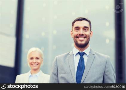 business, partnership, success and people concept - close up of smiling businessman and businesswoman standing over office building