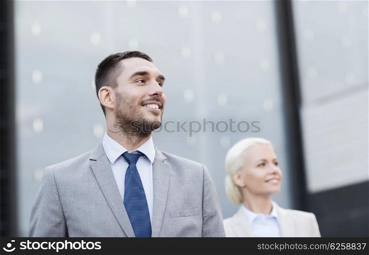 business, partnership, success and people concept - close up of smiling businessman and businesswoman standing over office building