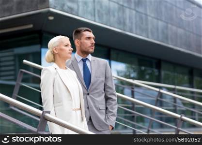 business, partnership, success and people concept - serious businessman and businesswoman standing over office building