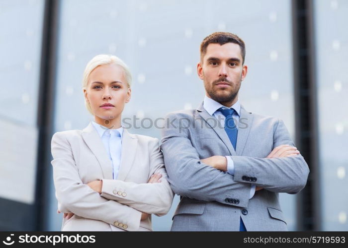 business, partnership, success and people concept - serious businessman and businesswoman standing over office building