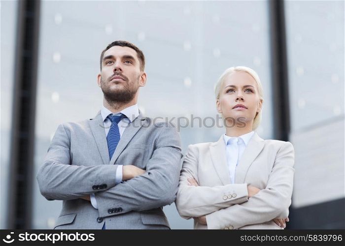 business, partnership, success and people concept - serious businessman and businesswoman standing over office building