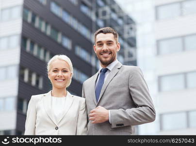 business, partnership, success and people concept - smiling businessman and businesswoman standing over office building