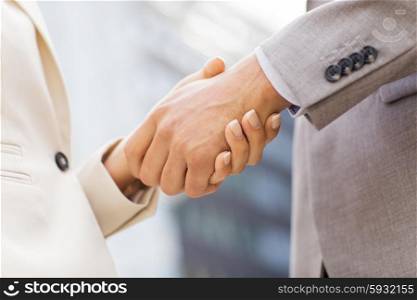 business, partnership, success, gesture and people concept - close up of business couple shaking hands on city street over office building