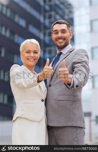 business, partnership, success, gesture and people concept - smiling businessman and businesswoman showing thumbs up over office building