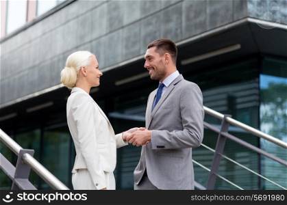 business, partnership, success, gesture and people concept - smiling businessman and businesswoman shaking hands on city street