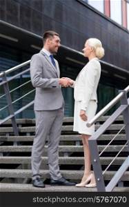 business, partnership, success, gesture and people concept - smiling businessman and businesswoman shaking hands on city street