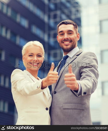 business, partnership, success, gesture and people concept - smiling businessman and businesswoman showing thumbs up over office building