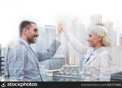 business, partnership, success, gesture and people concept - smiling businessman and businesswoman standing over dubai city background with double exposure effect