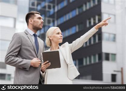 business, partnership, technology and people concept - serious businessman and businesswoman with tablet pc computer over office building