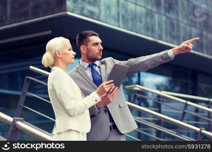 business, partnership, technology and people concept - serious businessman and businesswoman with tablet pc computer over office building