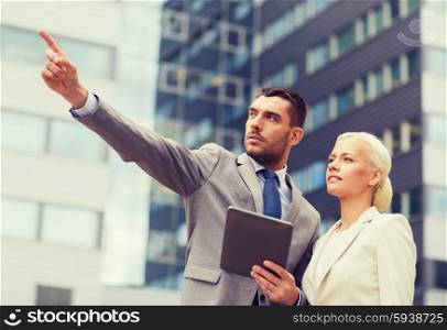 business, partnership, technology and people concept - serious businessman and businesswoman with tablet pc computer over office building