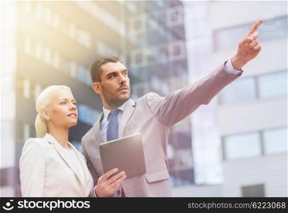 business, partnership, technology and people concept - serious businessman and businesswoman with tablet pc computer pointing finger to something over office building