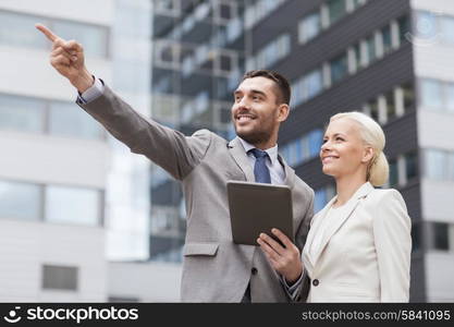 business, partnership, technology and people concept - smiling businessman and businesswoman with tablet pc computer over office building