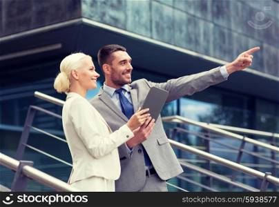 business, partnership, technology and people concept - smiling businessman and businesswoman with tablet pc computer over office building
