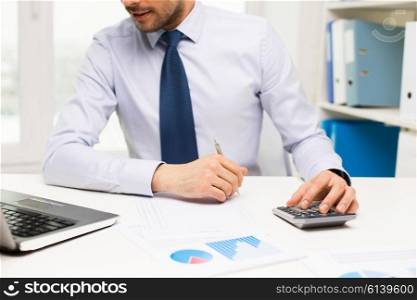 business, people, accounting and technology concept - close up of businessman with laptop computer, calculator and papers working in office