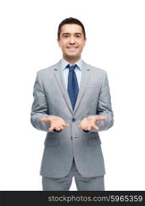 business, people, advertisement and office concept - happy businessman in suit showing or holding something imaginary on empty palms
