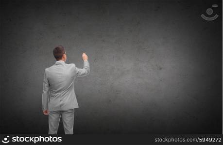 business, people, advertisement , information and office concept - businessman writing or drawing something imaginary from back over dark gray concrete wall background