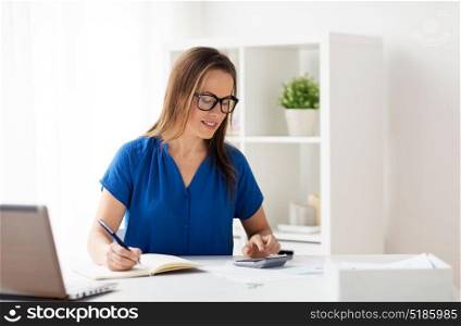 business, people and bookkeeping concept - woman with calculator counting and writing to notebook at office. woman with calculator and notebook at office