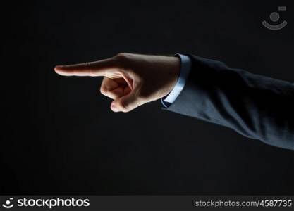 business, people and choice concept - close up of businessman hand pointing finger to something invisible over black background
