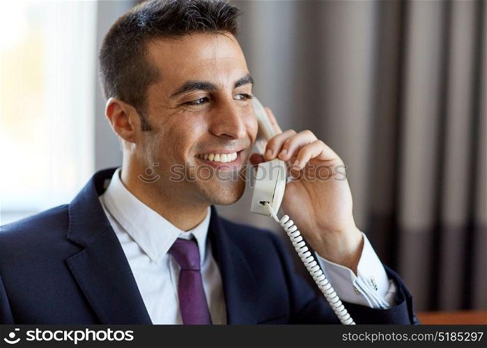 business, people and communication concept - close up of happy smiling businessman calling on desk phone at hotel room or office . businessman calling on phone at hotel or office