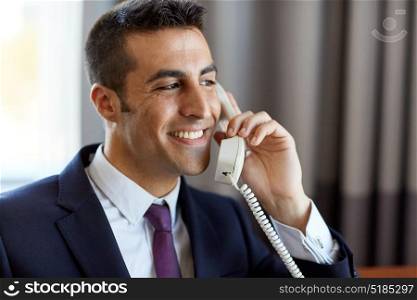 business, people and communication concept - close up of happy smiling businessman calling on desk phone at hotel room or office . businessman calling on phone at hotel or office