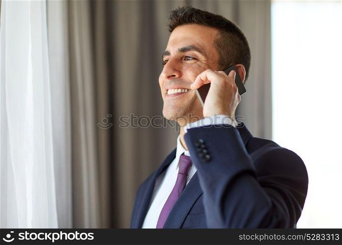 business, people and communication concept - happy smiling businessman calling on smartphone at hotel room or office . businessman calling on smartphone at hotel room