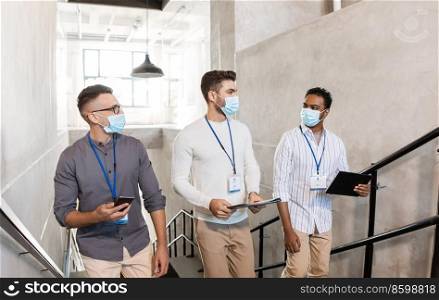 business, people and corporate concept - businessmen in masks with name tags walking up office stairs and talking. businessmen in masks with name tags going upstairs