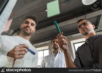 business, people and corporate concept - businessmen working with charts on glass board at office. men working with charts on glass board at office