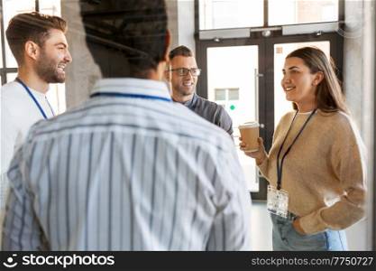 business, people and corporate concept - group of happy smiling colleagues with name tags drinking takeaway coffee at office. business people drinking takeaway coffee at office