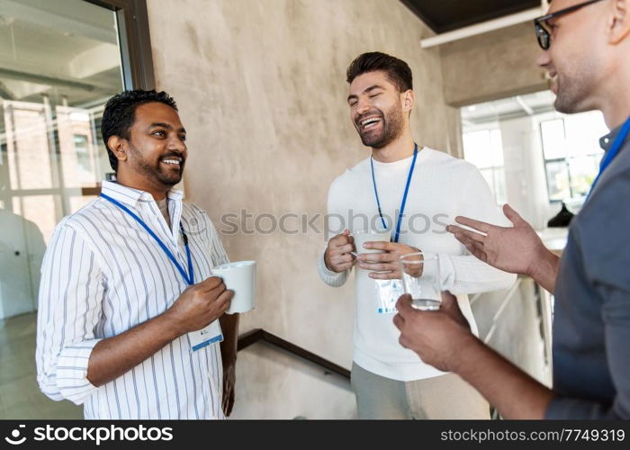 business, people and corporate concept - happy smiling businessmen or male colleagues with name tags drinking takeaway coffee at office. businessmen drinking takeaway coffee at office