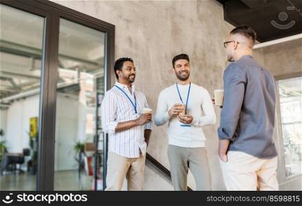 business, people and corporate concept - happy smiling businessmen or male colleagues with name tags drinking takeaway coffee at office. businessmen drinking takeaway coffee at office