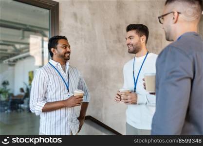 business, people and corporate concept - happy smiling businessmen or male colleagues with name tags drinking takeaway coffee at office. businessmen drinking takeaway coffee at office
