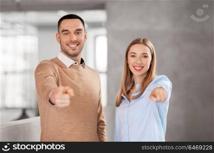 business, people and corporate concept - happy smiling businesswoman and businessman pointing at you at office. businesswoman and businessman pointing at you