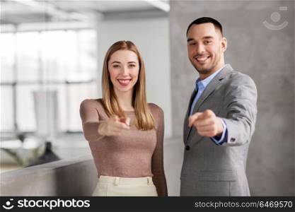 business, people and corporate concept - happy smiling businesswoman and businessman pointing at you at office. businesswoman and businessman pointing at you
