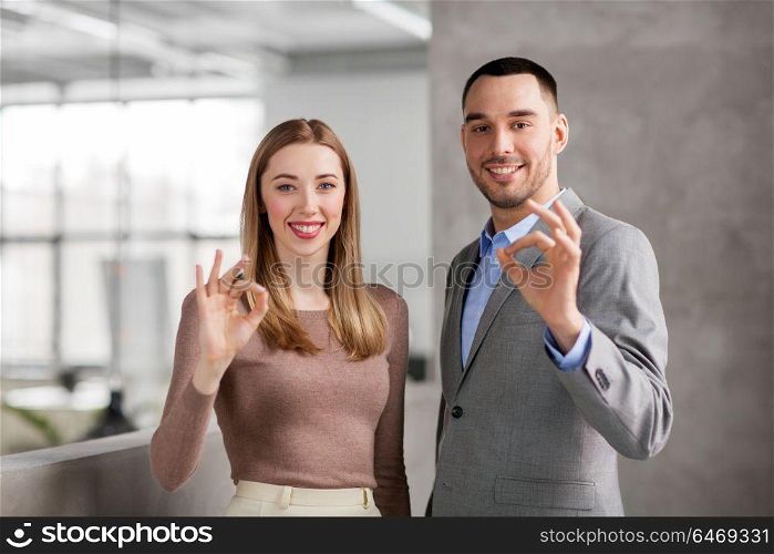 business, people and corporate concept - happy smiling businesswoman and businessman showing ok hand sign at office. businesswoman and businessman showing ok at office