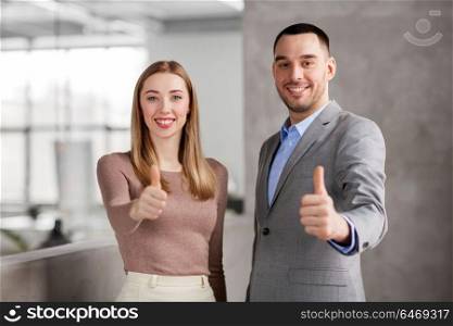 business, people and corporate concept - happy smiling businesswoman and businessman showing thumbs up at office. businesswoman and businessman showing thumbs up
