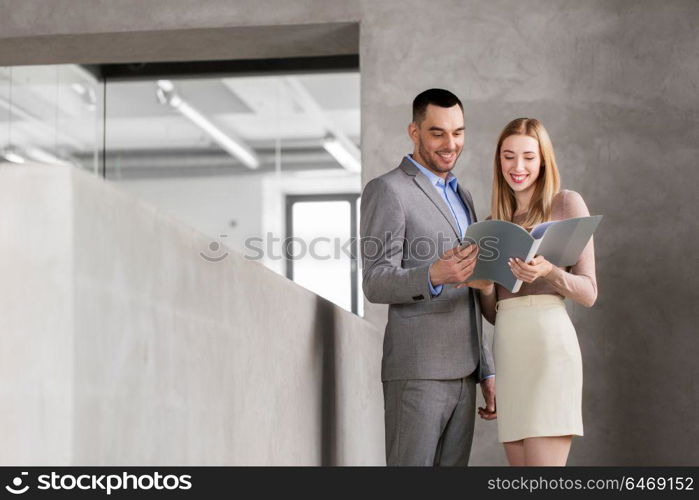 business, people and corporate concept - happy smiling businesswoman and businessman with folder at office. businesswoman and businessman with folder