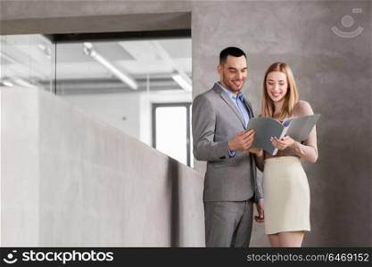business, people and corporate concept - happy smiling businesswoman and businessman with folder at office. businesswoman and businessman with folder
