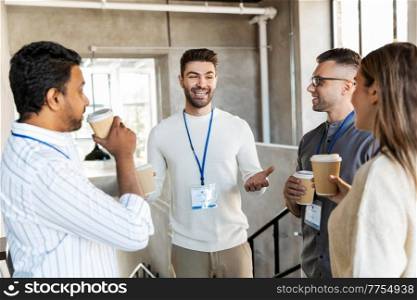 business, people and corporate concept - happy smiling colleagues with name tags drinking takeaway coffee at office. business people drinking takeaway coffee at office