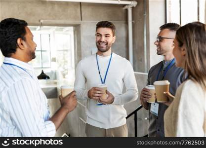 business, people and corporate concept - happy smiling colleagues with name tags drinking takeaway coffee at office. business people drinking takeaway coffee at office