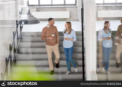 business, people and corporate concept - happy smiling man and woman drinking coffee and walking down office stairs. man and woman with coffee at office stairs