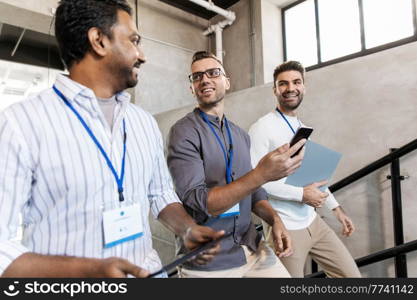 business, people and corporate concept - men with conference badges, folder, tablet pc computer and smartphone walking up office stairs. men with conference badges walking upstairs